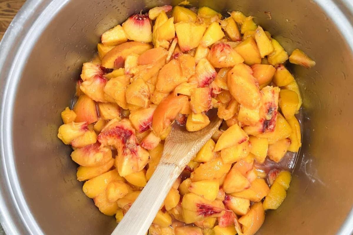 Chopped fresh peaches in a large pot with a wooden spoon, ready for cooking or making preserves.