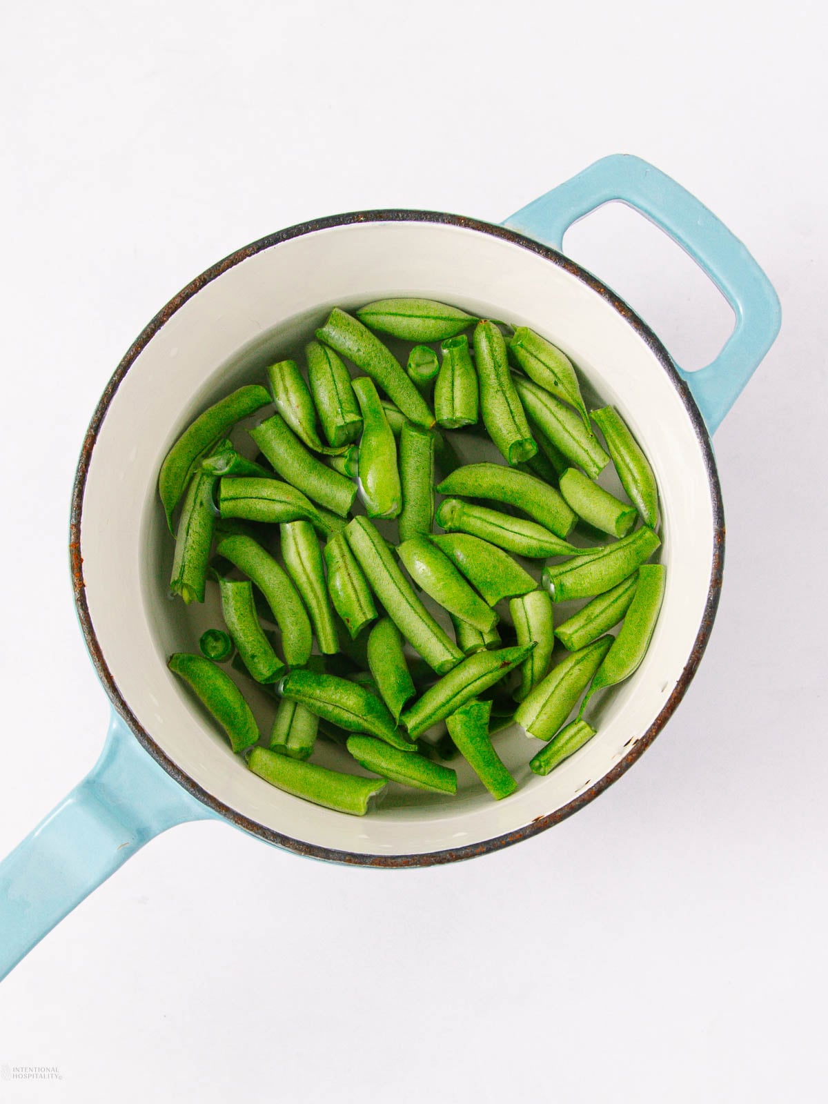 Light blue pot filled with fresh, chopped green beans, set against a white background.