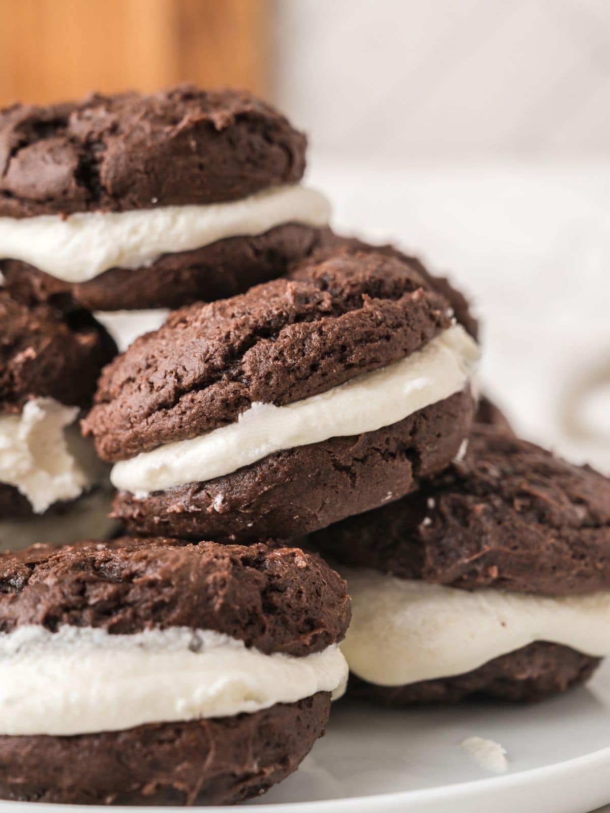 A close-up of chocolate sandwich cookies with white cream filling, stacked on a white plate.