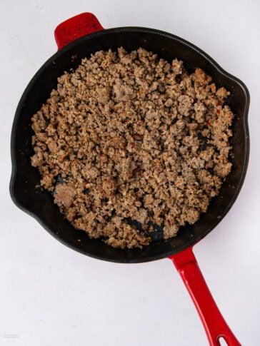 Cooked ground beef in a black cast iron skillet with a red handle, placed on a white surface.