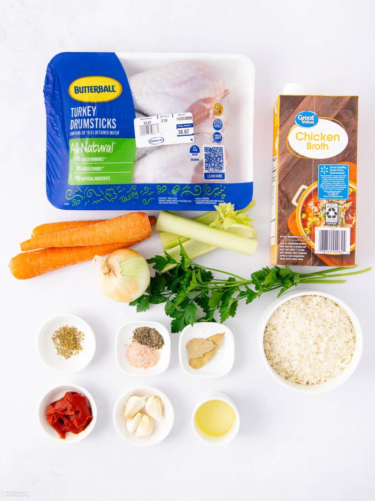 Ingredients for turkey soup including turkey drumsticks, chicken broth, carrots, celery, onion, parsley, rice, tomato paste, garlic, spices, and oil, all displayed neatly on a white surface.