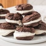 A plate of chocolate whoopie pies with white cream filling, stacked on top of each other on a white surface.