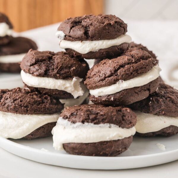 A plate of chocolate whoopie pies with white cream filling, stacked on top of each other on a white surface.