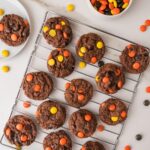 Chocolate cookies topped with orange and yellow candy pieces on a metal cooling rack, with a bowl of the candies nearby.