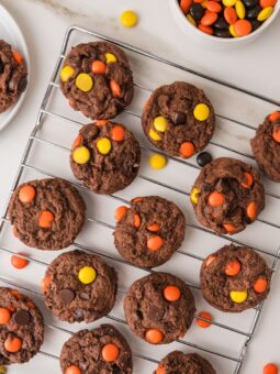 Chocolate cookies topped with orange and yellow candy pieces on a metal cooling rack, with a bowl of the candies nearby.