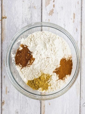 A glass bowl containing a mound of white flour topped with three piles of different colored spices.