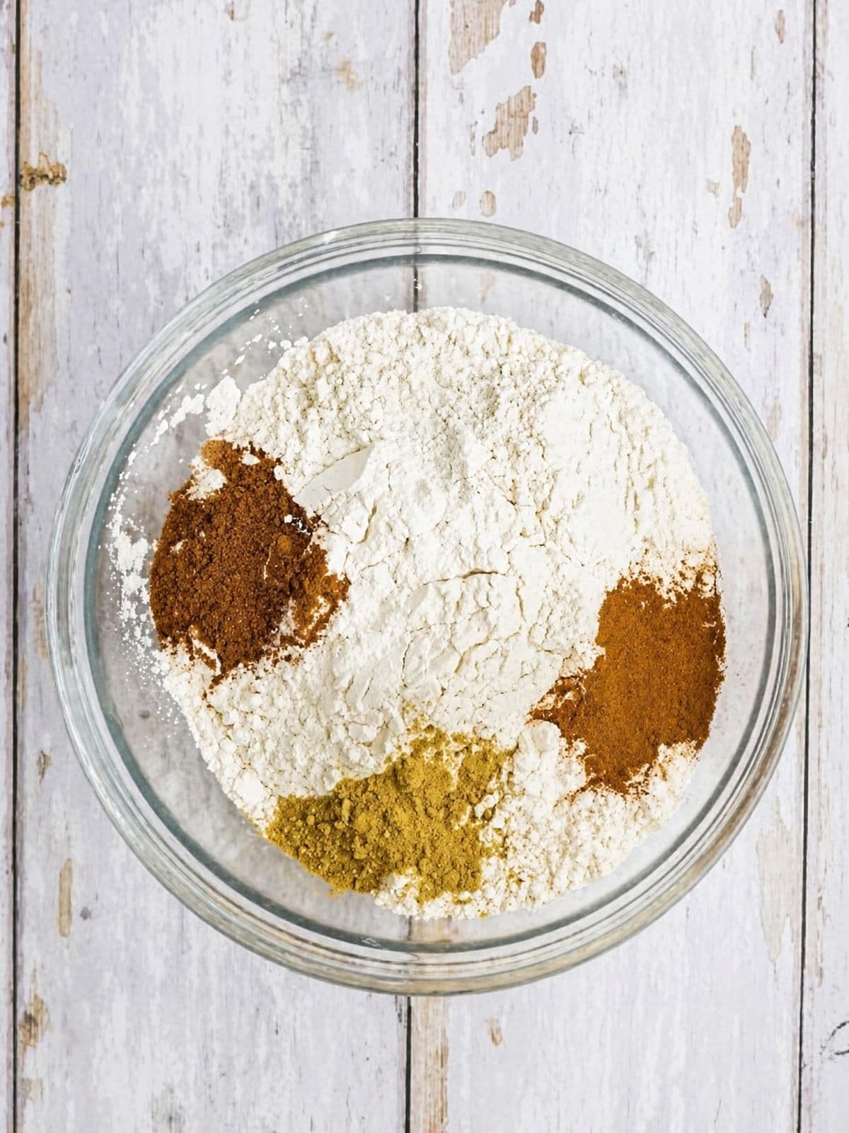 A glass bowl containing a mound of white flour topped with three piles of different colored spices.