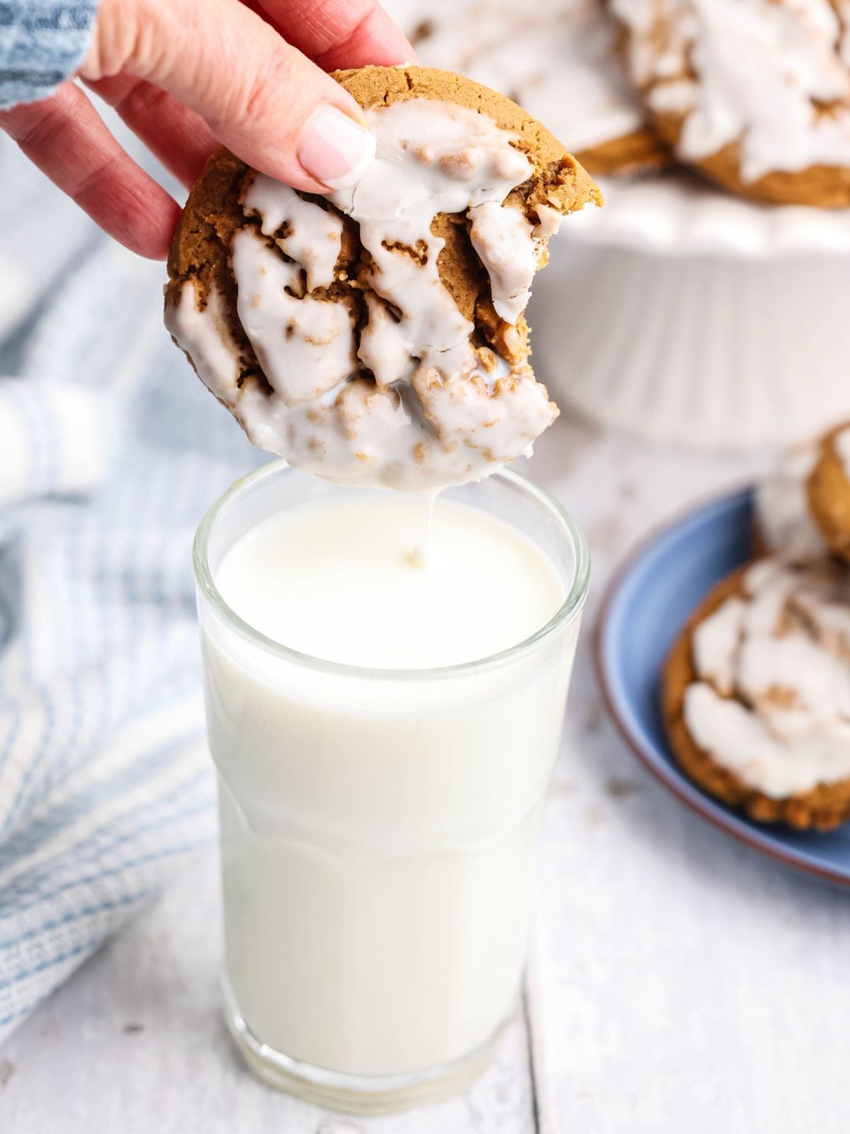 A hand dips a bitten, glazed cookie into a glass of milk.