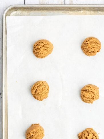 Five scoops of cookie dough arranged on a parchment-lined baking sheet.