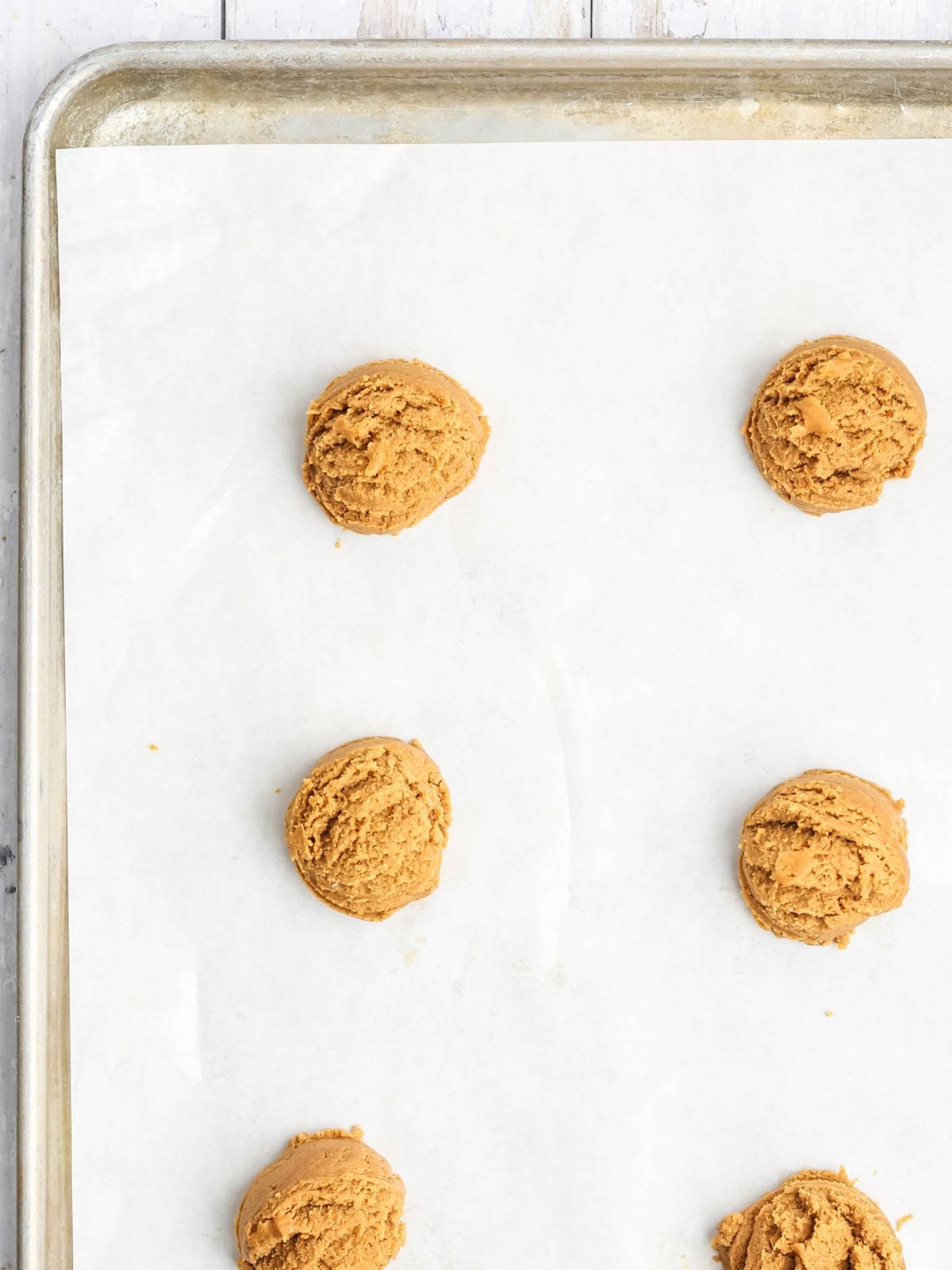 Five scoops of cookie dough arranged on a parchment-lined baking sheet.