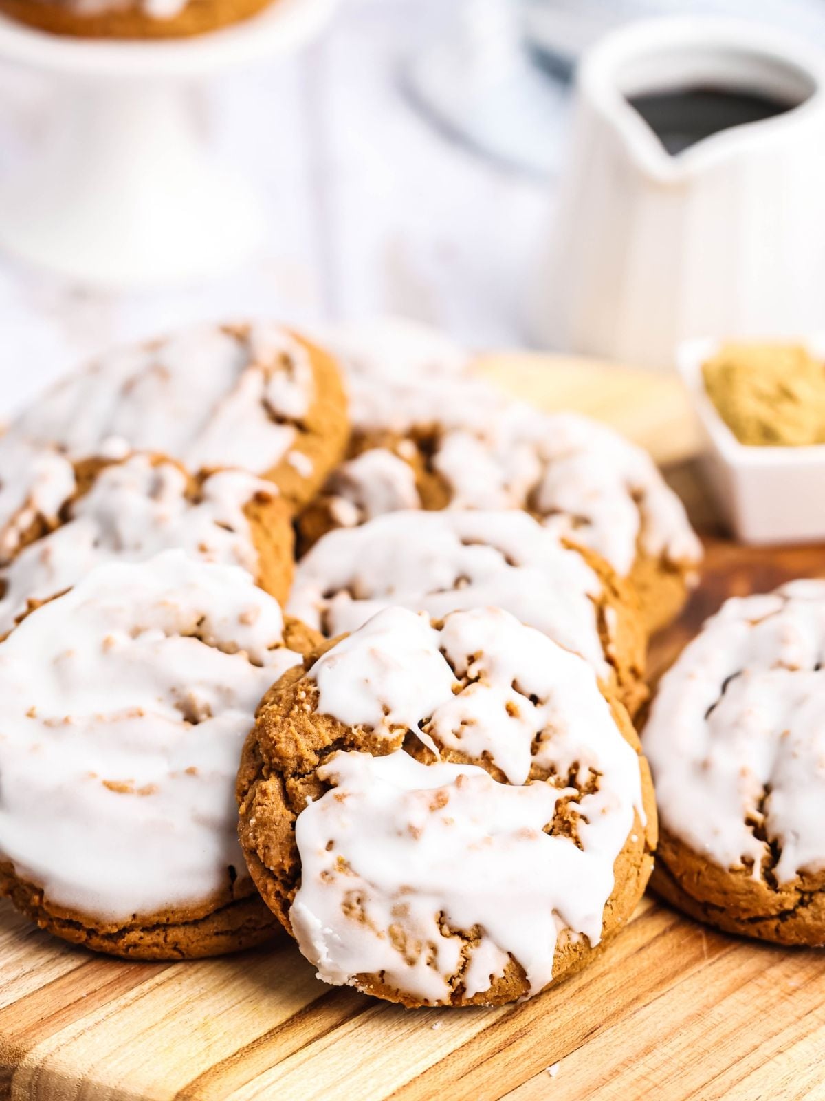 A pile of glazed spice cookies on a wooden cutting board.