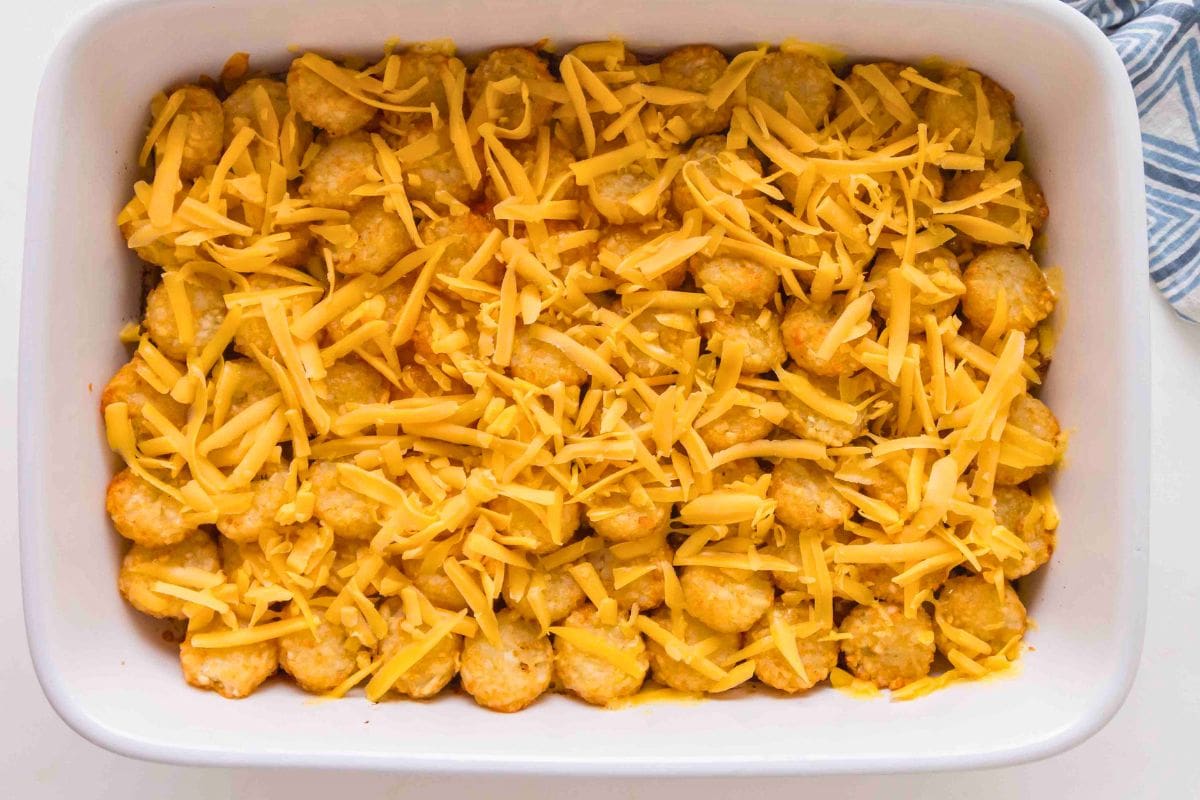 A casserole dish filled with a layer of tater tots topped with shredded cheddar cheese.