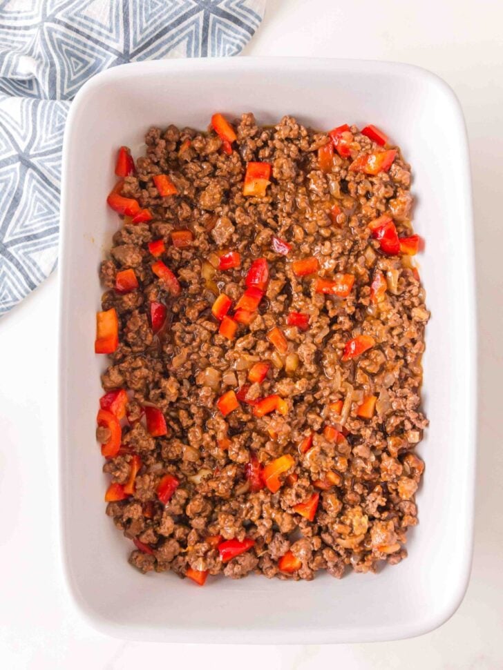 A white baking dish filled with a mixture of cooked ground meat and diced red bell peppers.