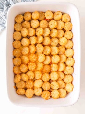 A rectangular white baking dish filled with a casserole topped with a single, uniform layer of golden-brown tater tots.