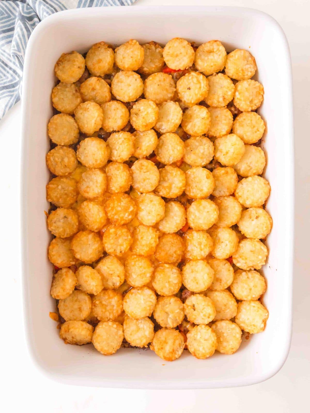 A rectangular white baking dish filled with a casserole topped with a single, uniform layer of golden-brown tater tots.