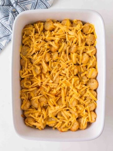 A rectangular baking dish filled with tater tots topped with shredded cheddar cheese.