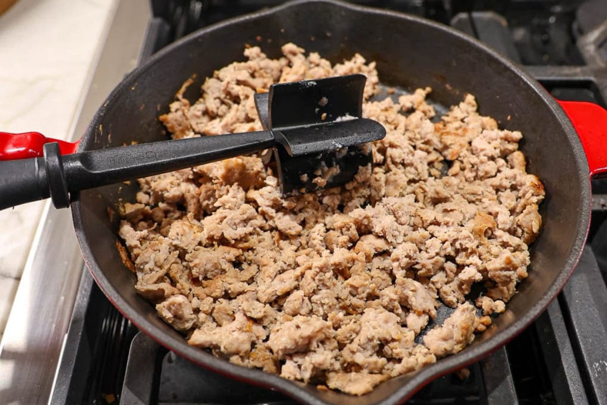 Ground meat cooking in a cast iron skillet with a black meat chopper tool.