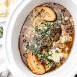 French onion soup topped with melted cheese, fresh herbs, and toasted baguette slices in a slow cooker.