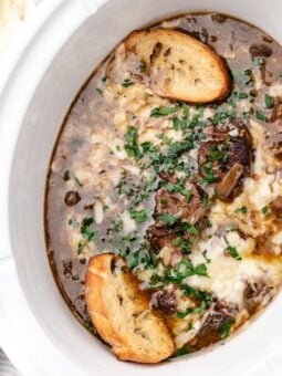 French onion soup topped with melted cheese, fresh herbs, and toasted baguette slices in a slow cooker.