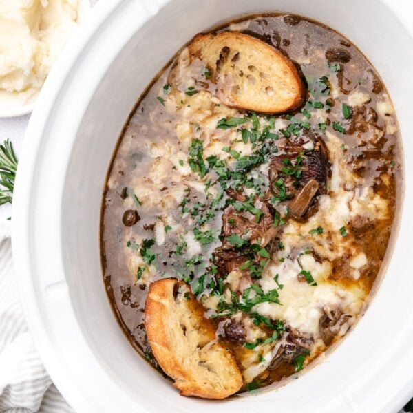French onion soup topped with melted cheese, fresh herbs, and toasted baguette slices in a slow cooker.