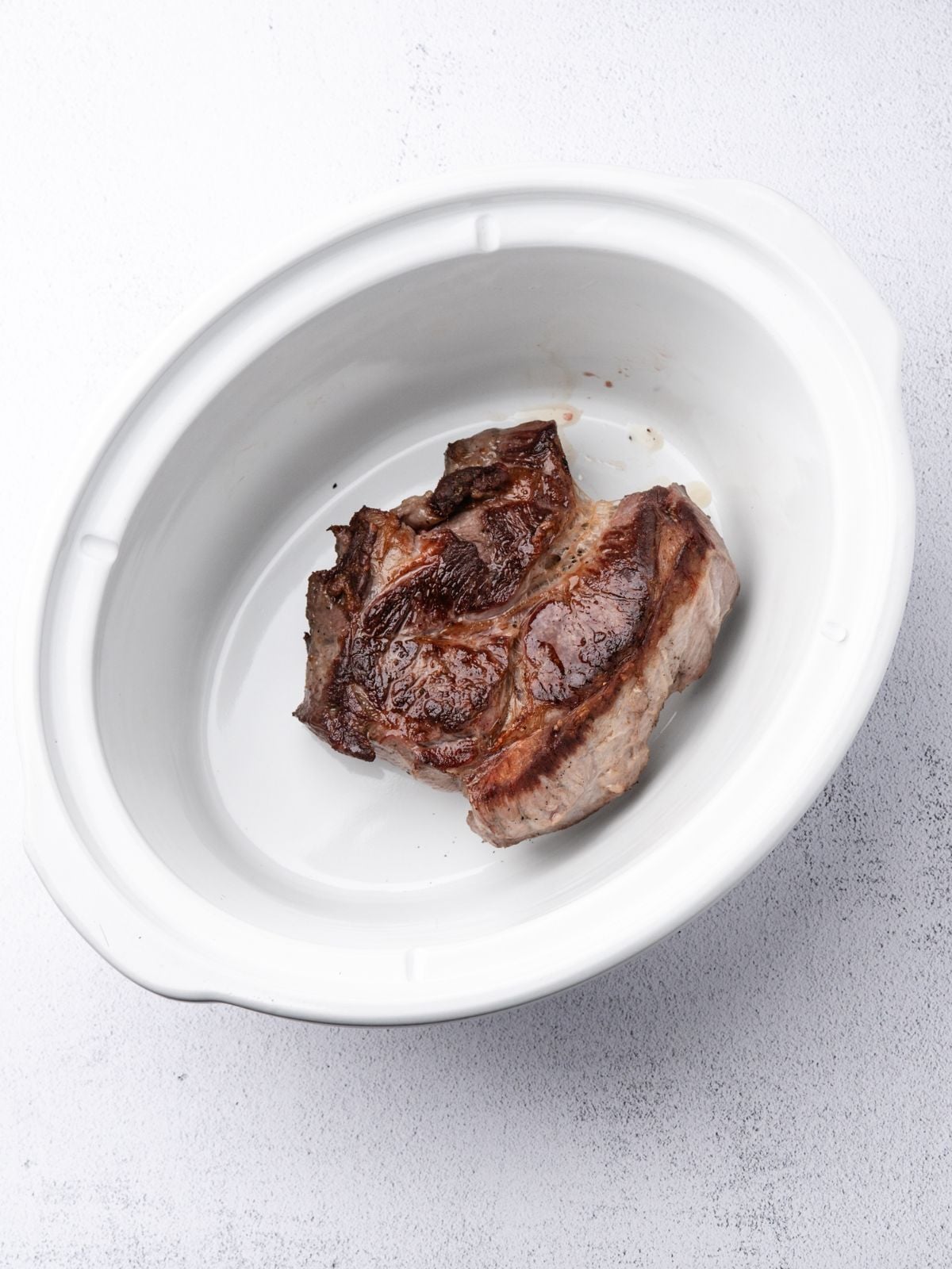 A seared piece of meat in a white oval ceramic dish.