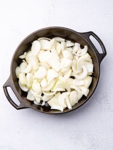 Sliced white onions in a cast-iron skillet.