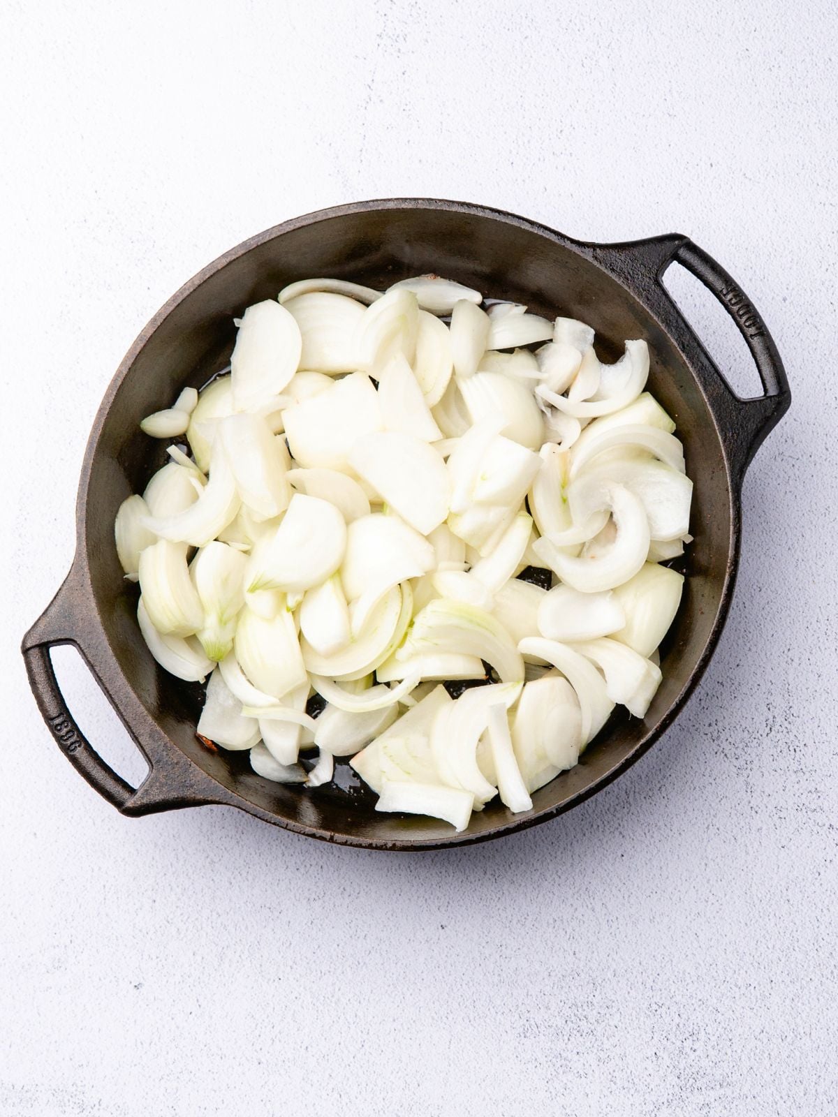 Sliced white onions in a cast-iron skillet.