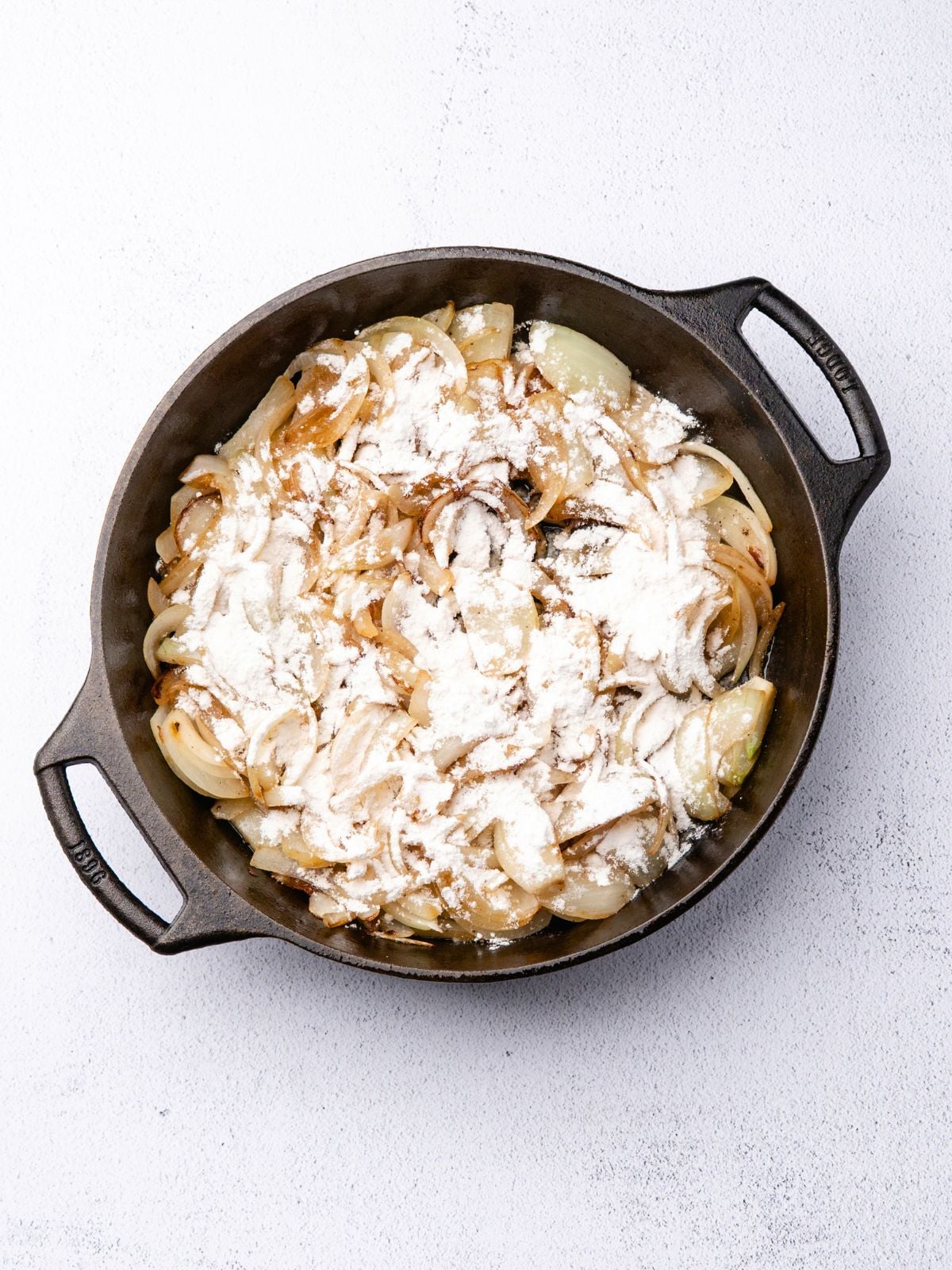 Sautéed sliced onions dusted with flour in a black cast iron skillet.
