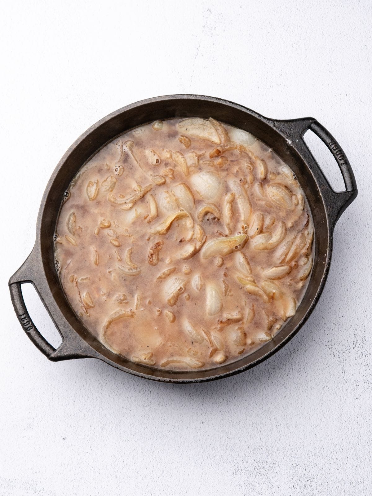 Sliced onions sautéing in a cast iron skillet.