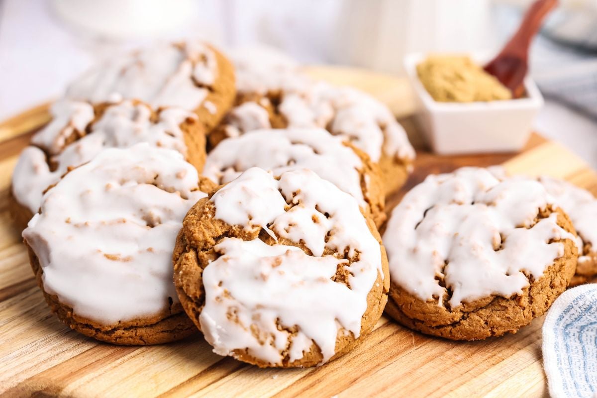 A group of iced spice cookies on a wooden cutting board.