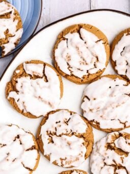 Glazed round cookies on a white platter, with a partially eaten cookie on a blue plate nearby.