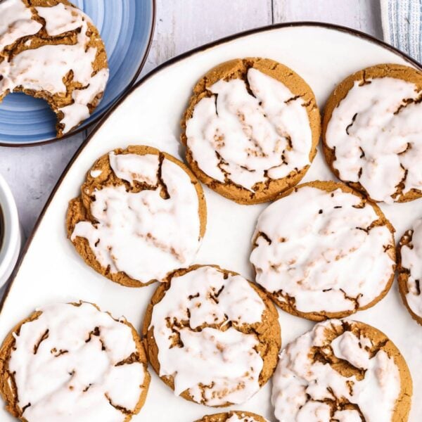 Glazed round cookies on a white platter, with a partially eaten cookie on a blue plate nearby.